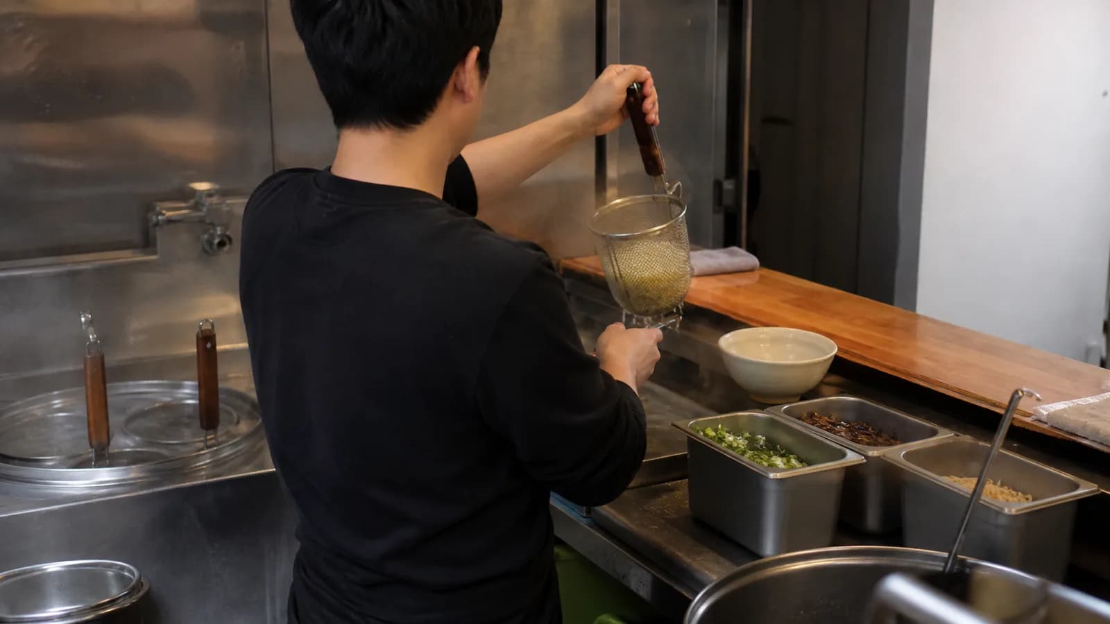 좁은 라면 주방에서 면솥의 면 바구니를 들어 올리는 조리자